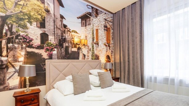 Habitación de hotel con cama, mesita de noche, lámpara y vista a la calle a través de la ventana.