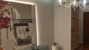 Una sala de estar con un sofá gris, una mesa de centro redonda, una araña de techo y un muro decorativo con estampado floral.