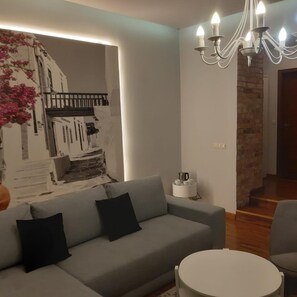 Una sala de estar con un sofá gris, una mesa de centro redonda, una araña de techo y un muro decorativo con estampado floral.
