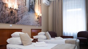 Hotelkamer met twee bedden, een groot schilderij van een straat, een raam met gordijnen en een stoel.