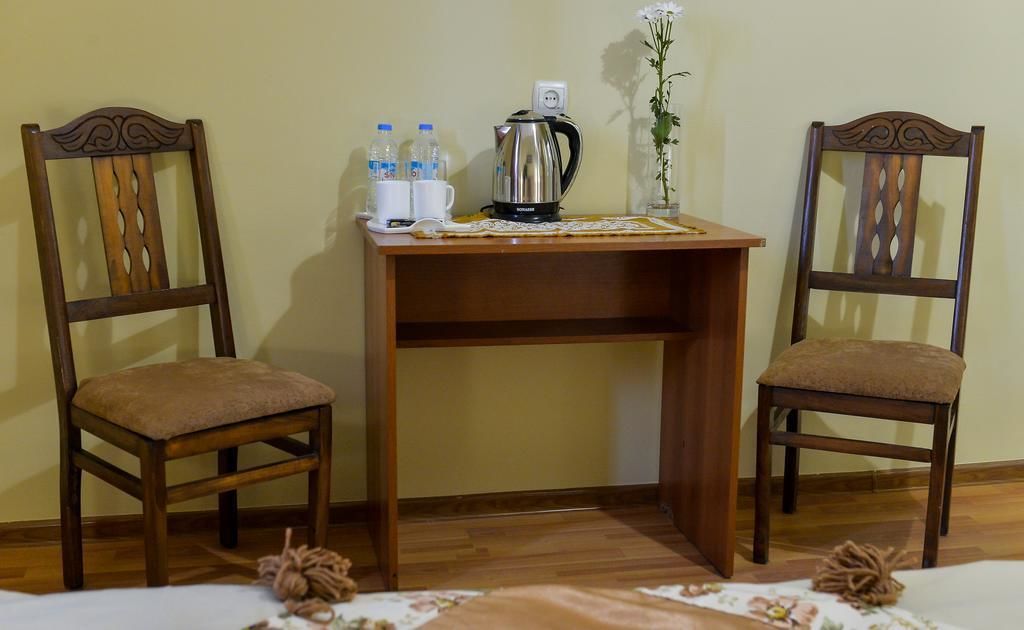 A small wooden desk with two chairs, a kettle, water bottles, and a vase with a flower.