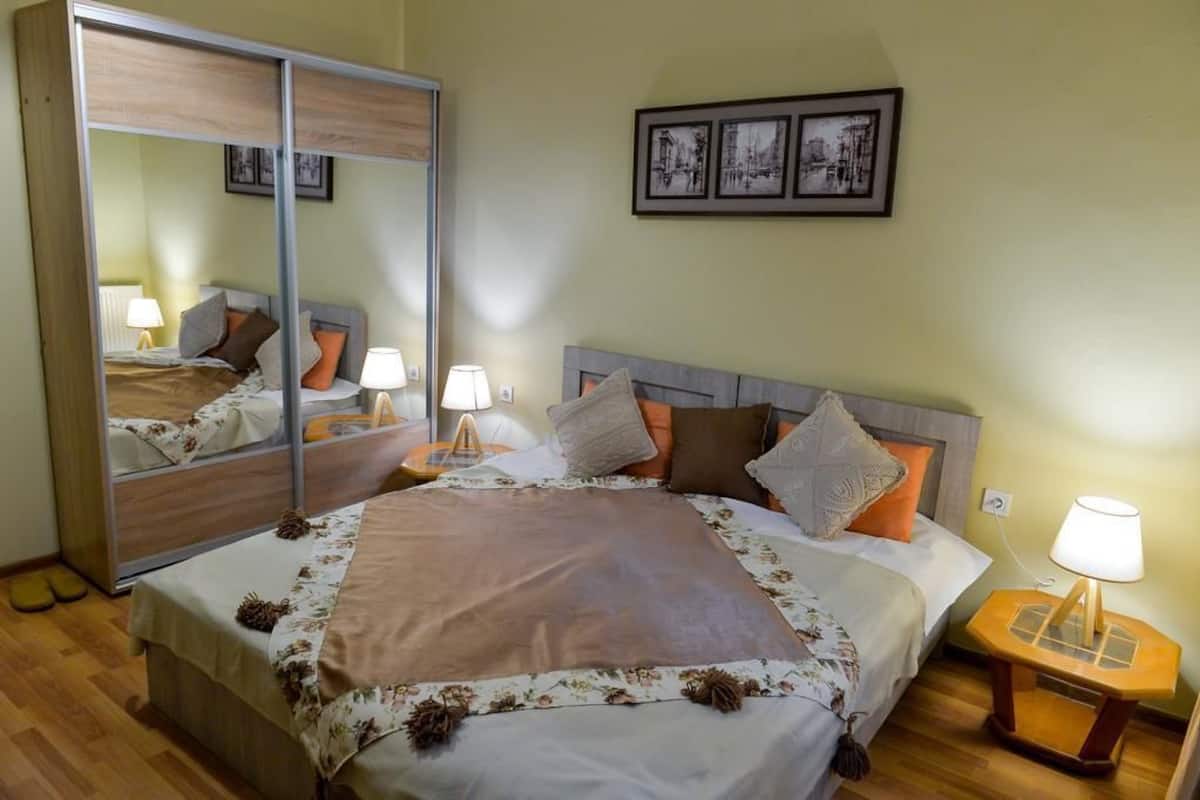 A neatly arranged bedroom with a bed, bedside lamps, a mirror, and framed pictures on the wall.