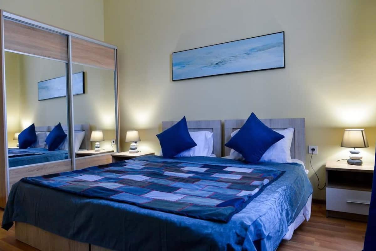 A hotel room with a large bed, two bedside tables, a mirror, a painting on the wall, and a wooden floor.