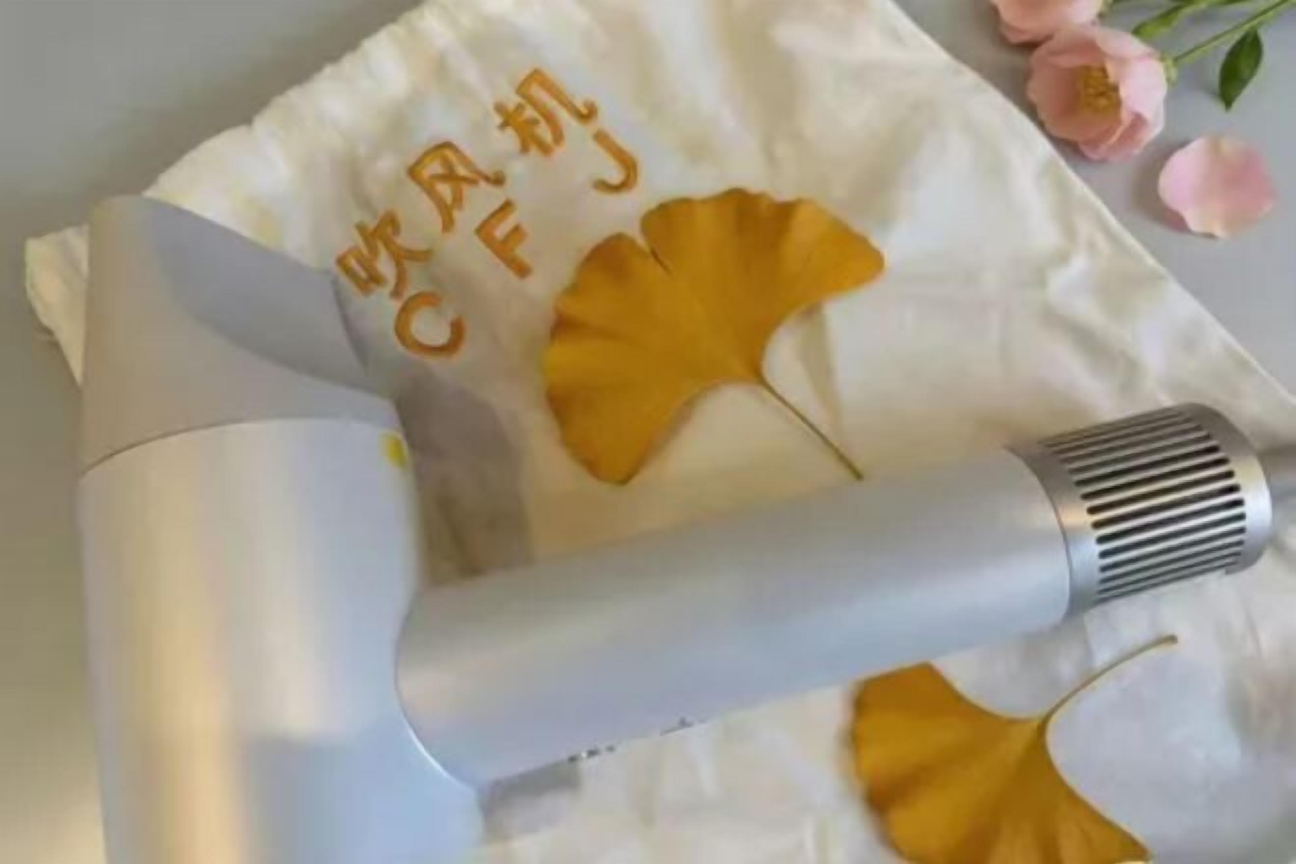 A white towel with yellow ginkgo leaves and Chinese characters, a white hairdryer, and pink flowers.