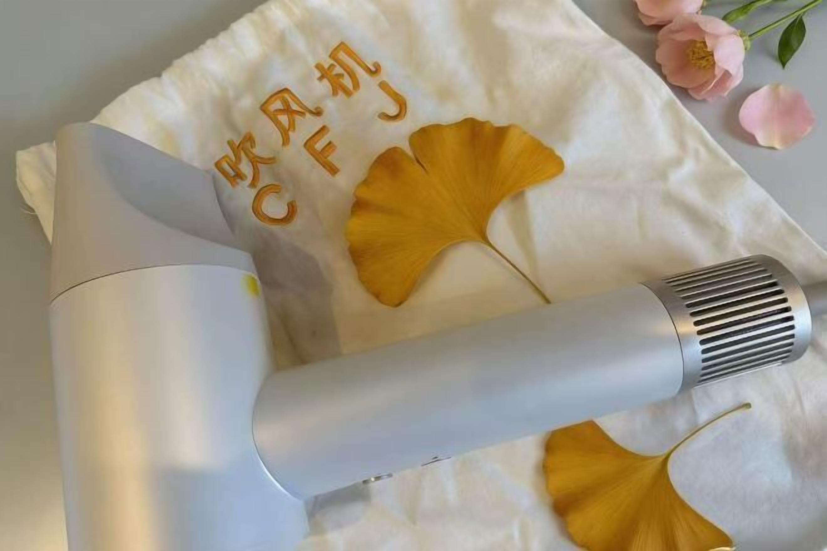 A hair dryer on a white towel with Chinese characters and ginkgo leaves.