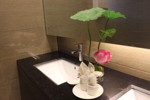 A bathroom with a black countertop, a white sink, a mirror, and a green plant with a pink flower. - Jianchuan Hotel (Jianchuan)