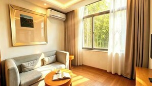 A living room with a sofa, a round table with a book, a framed picture on the wall, and a window with curtains. - Jianchuan Hotel (Jianchuan)
