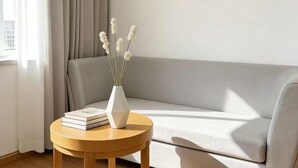 A room with a sofa, a round wooden table with a white vase and books, and a window with curtains. - Jianchuan Hotel (Jianchuan)