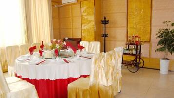 A dining area with a round table set for a meal, surrounded by chairs with white and red tablecloths.