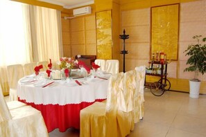 A dining area with a round table set for a meal, surrounded by chairs with white and red tablecloths. - Jianchuan Hotel (Jianchuan)