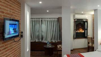 Ein Hotelzimmer mit Backsteinwand, einem daran befestigten Fernseher, einem Fenster mit Vorhängen, einem kleinen runden Tisch mit einem Stuhl und einem Bett mit rot-weißer Bettdecke.