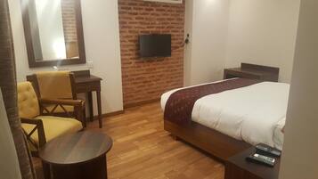 Habitación de hotel con una cama, un escritorio, una silla, un televisor montado en una pared de ladrillo y piso de madera.