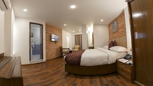 Ein Hotelzimmer mit einem runden Bett, Holzboden, einem an der Wand befestigten Fernseher, einem Schreibtisch mit Telefon und einem Kleiderschrank.