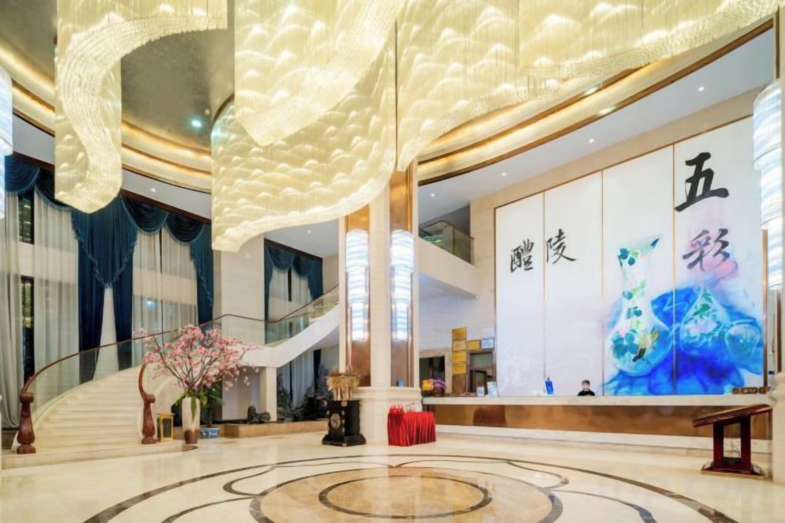 Un amplio vestíbulo con una imponente escalera, un mostrador de recepción y una gran pared con detalles decorativos.