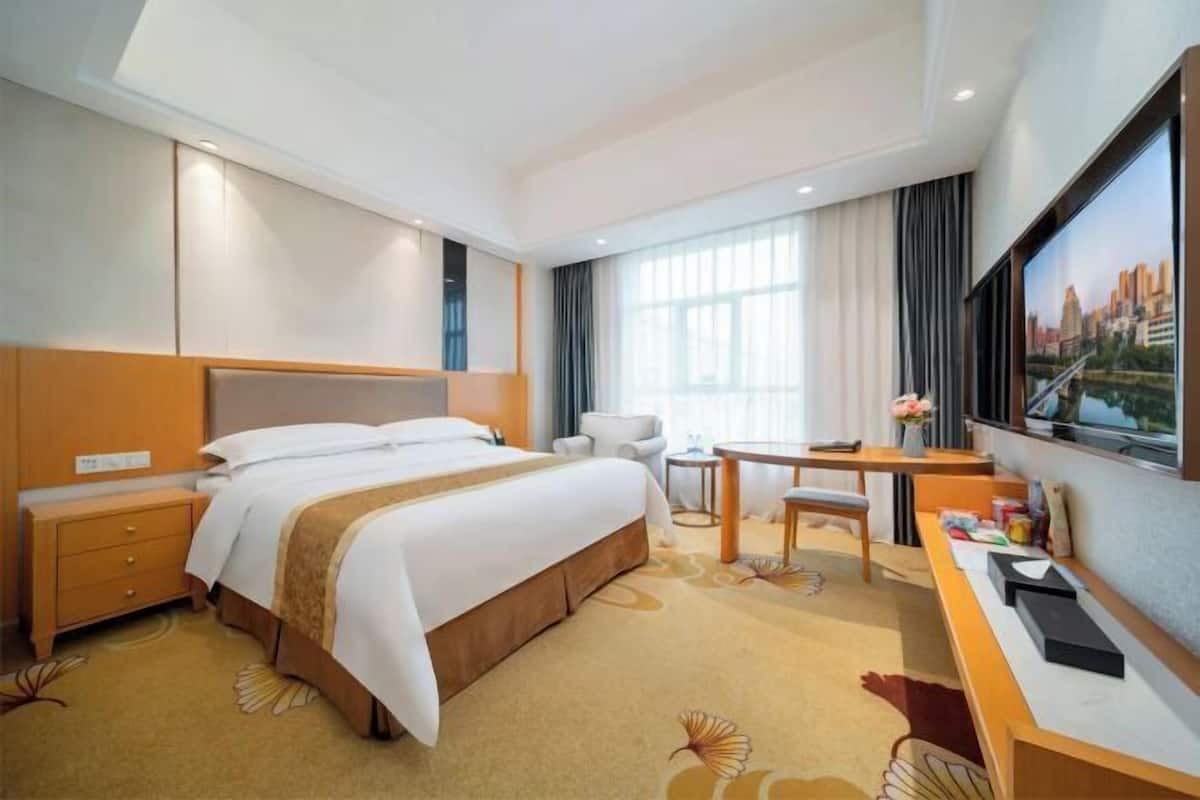 A hotel room with a bed, desk, chair, and a large window with curtains.