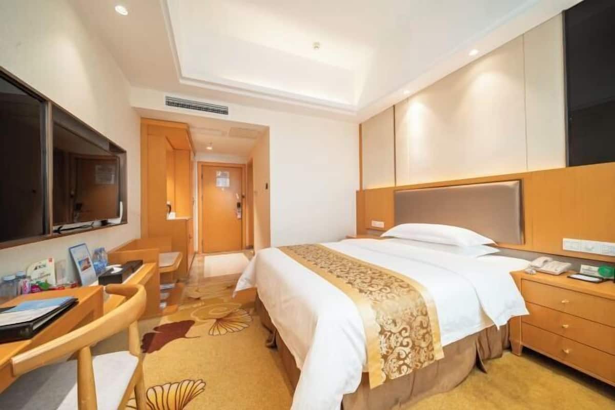 A hotel room with a bed, desk, chair, TV, and a door leading to another room.