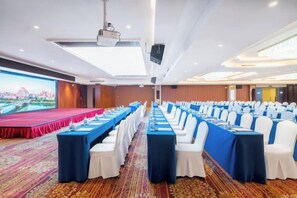 A conference room with a stage, rows of tables with white chairs, and a large screen. - Dongfeng Hotel (Liling)
