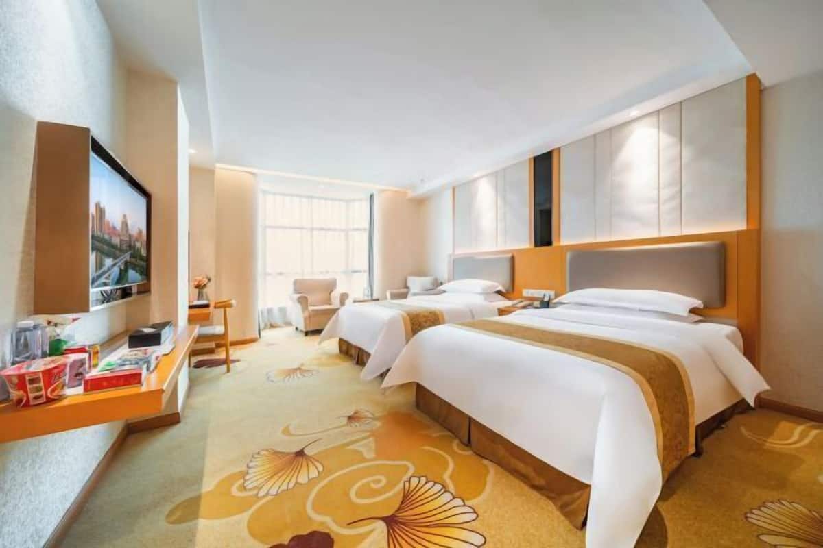 A hotel room with two beds, a TV, a desk with a chair, and a large window.