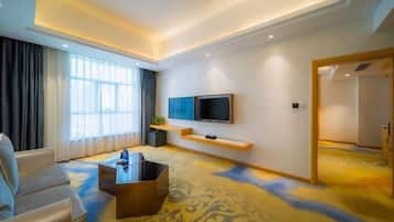 Ein modernes Hotelzimmer mit einer Couch, einem Couchtisch, einem an der Wand befestigten Fernseher und einem gemusterten Teppich.