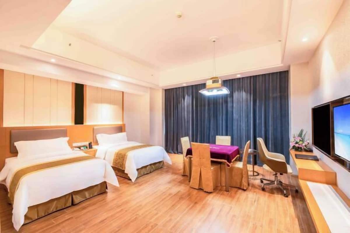 A hotel room with two beds, a desk, a chair, a TV, and a large window with curtains.