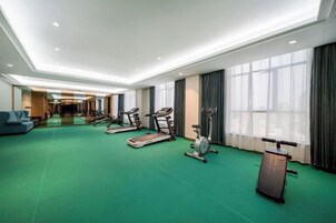 A hotel fitness room with exercise equipment, a green carpet, and large windows.