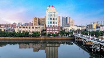 A cityscape with a prominent building reflecting on calm water, a bridge, and a clear sky.