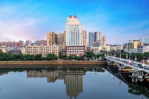 A cityscape with a prominent building reflecting on calm water, a bridge, and a clear sky.