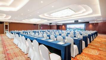 A conference room with rows of tables and chairs, a carpeted floor, and a large screen at the front.
