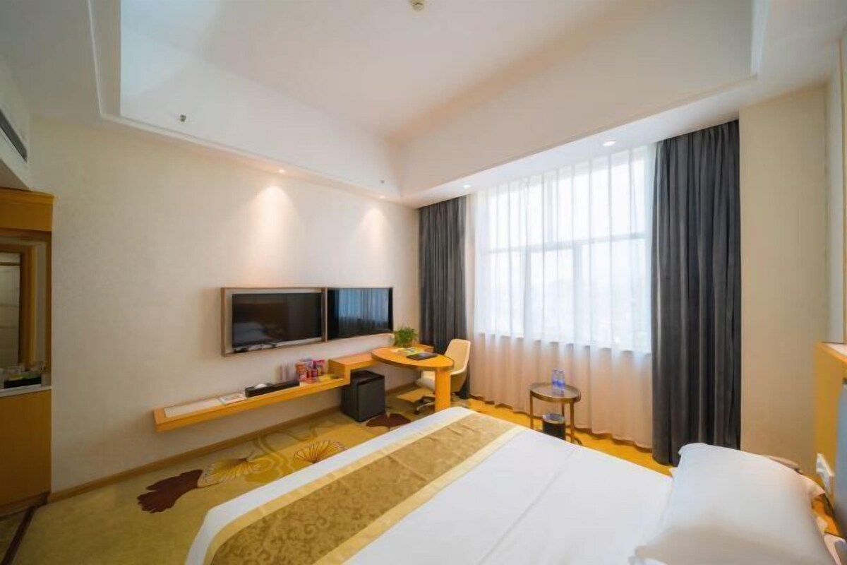 Een hotelkamer met een bed, een bureau, een televisie en een raam met gordijnen.