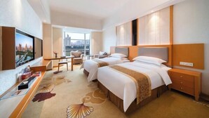 A hotel room with two beds, a desk, a TV, and a view of a cityscape.