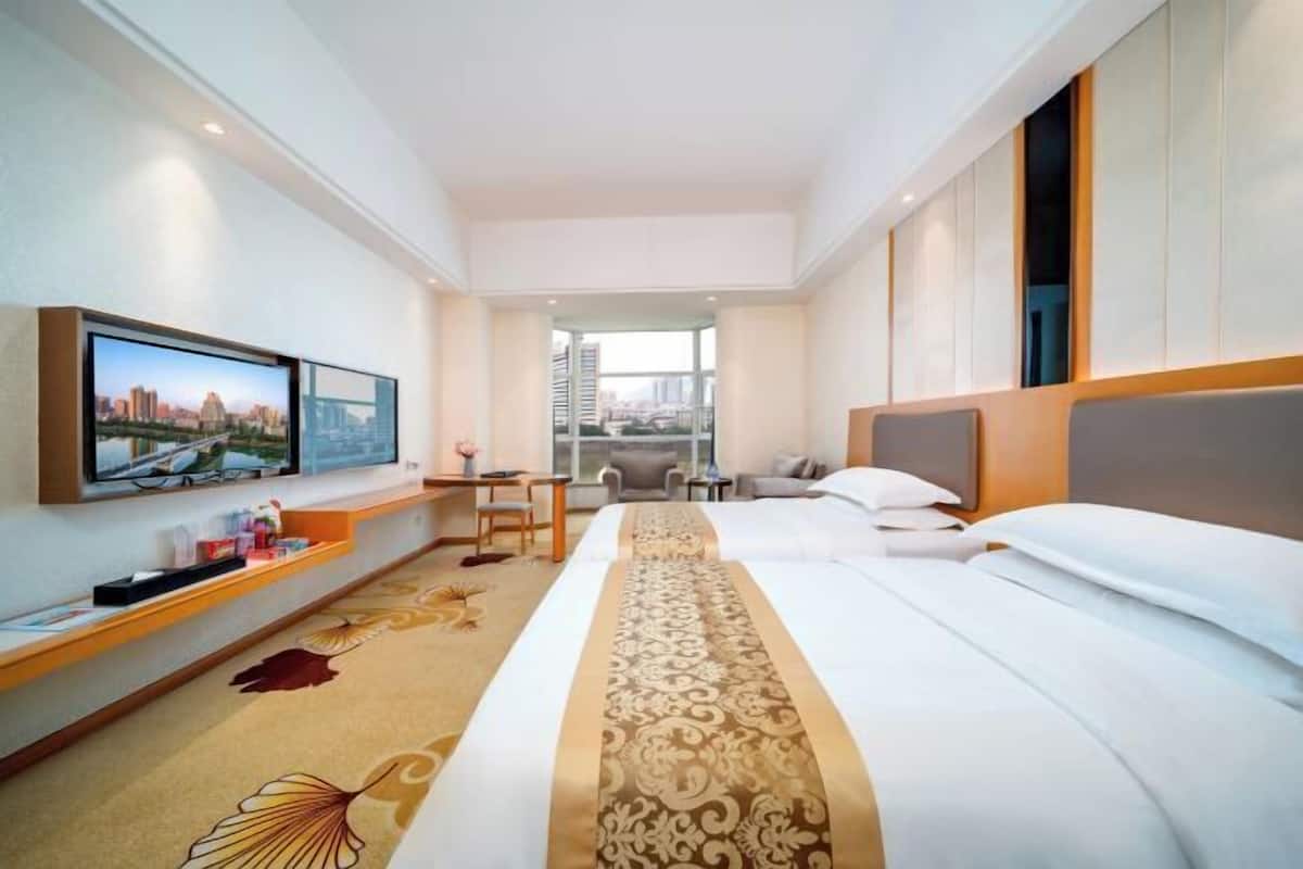 A hotel room with a bed, a TV, a desk, and a view of the city.