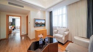 A hotel room with a flat-screen TV, a sofa, a coffee table, and a view of a cityscape through the window.