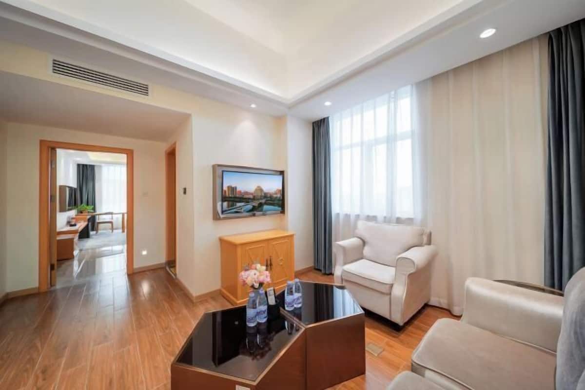 A hotel room with a flat-screen TV, a sofa, a coffee table, and a view of a cityscape through the window.