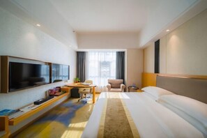Een moderne hotelkamer met een groot bed, een flatscreen televisie aan de muur, een bureau met stoel en een raam met gordijnen.