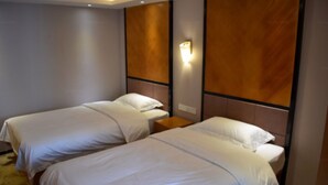 Habitación de hotel con dos camas individuales, cabecera de madera, mesita de noche y lámpara fijada a la pared.
