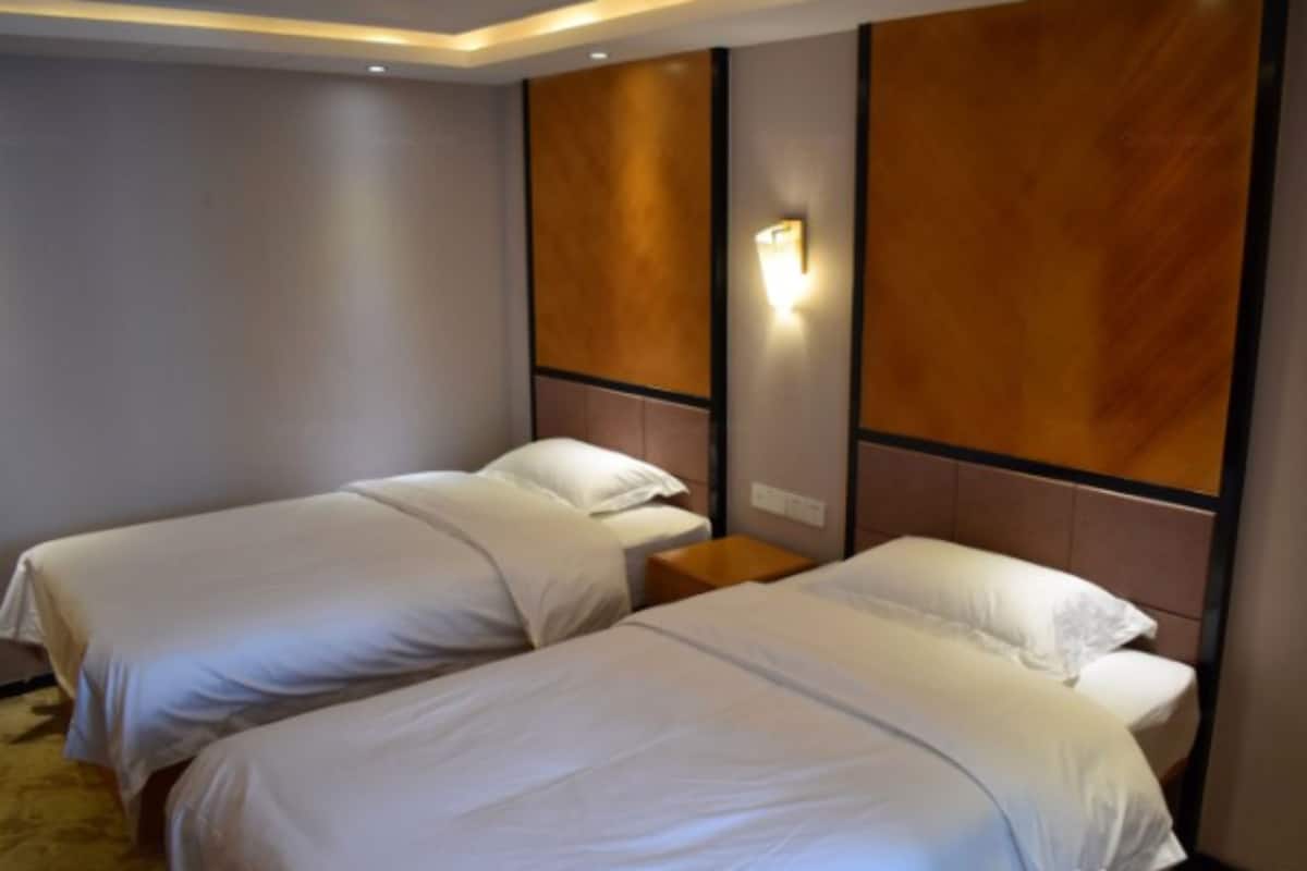A hotel room with two single beds, a wooden headboard, a nightstand, and a wall-mounted light fixture.
