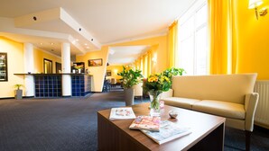 A hotel lobby with a reception desk, a sofa, a coffee table with magazines, and a vase of flowers. - Hotel Mirage (Duisburg)