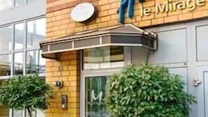 A hotel entrance with a sign reading 'Hotel le Mirage,' a glass door, and two potted plants. - Hotel Mirage (Duisburg)