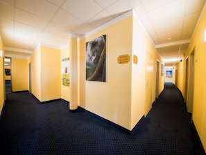 Pasillo de hotel con paredes amarillas, un cuadro grande de un oso y señales direccionales para las habitaciones 201-209 y 210-211.