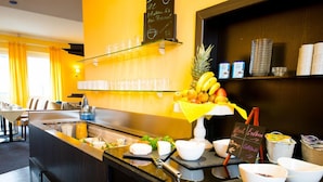 A hotel breakfast bar with a fruit display, coffee and tea options, and a chalkboard menu. - Hotel Mirage (Duisburg)