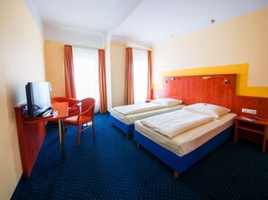Una habitación de hotel con dos camas, un escritorio con televisor y una silla.
