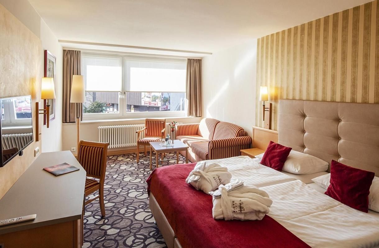 Ein Hotelzimmer mit Bett, Schreibtisch, Stuhl, Sofa, Tisch und einem fensterbepflanzten Fenster.