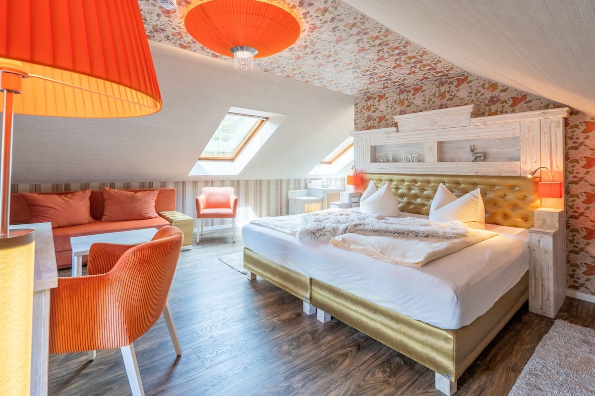 A bedroom with a large bed, a desk, and a chair. There is a skylight and a chandelier.