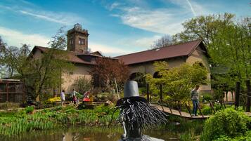 A historic building with a tower, surrounded by a garden with a pond and walking paths.