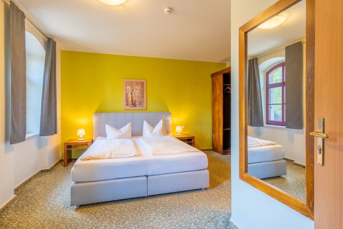A hotel room with a bed, bedside tables, a mirror, and a window.