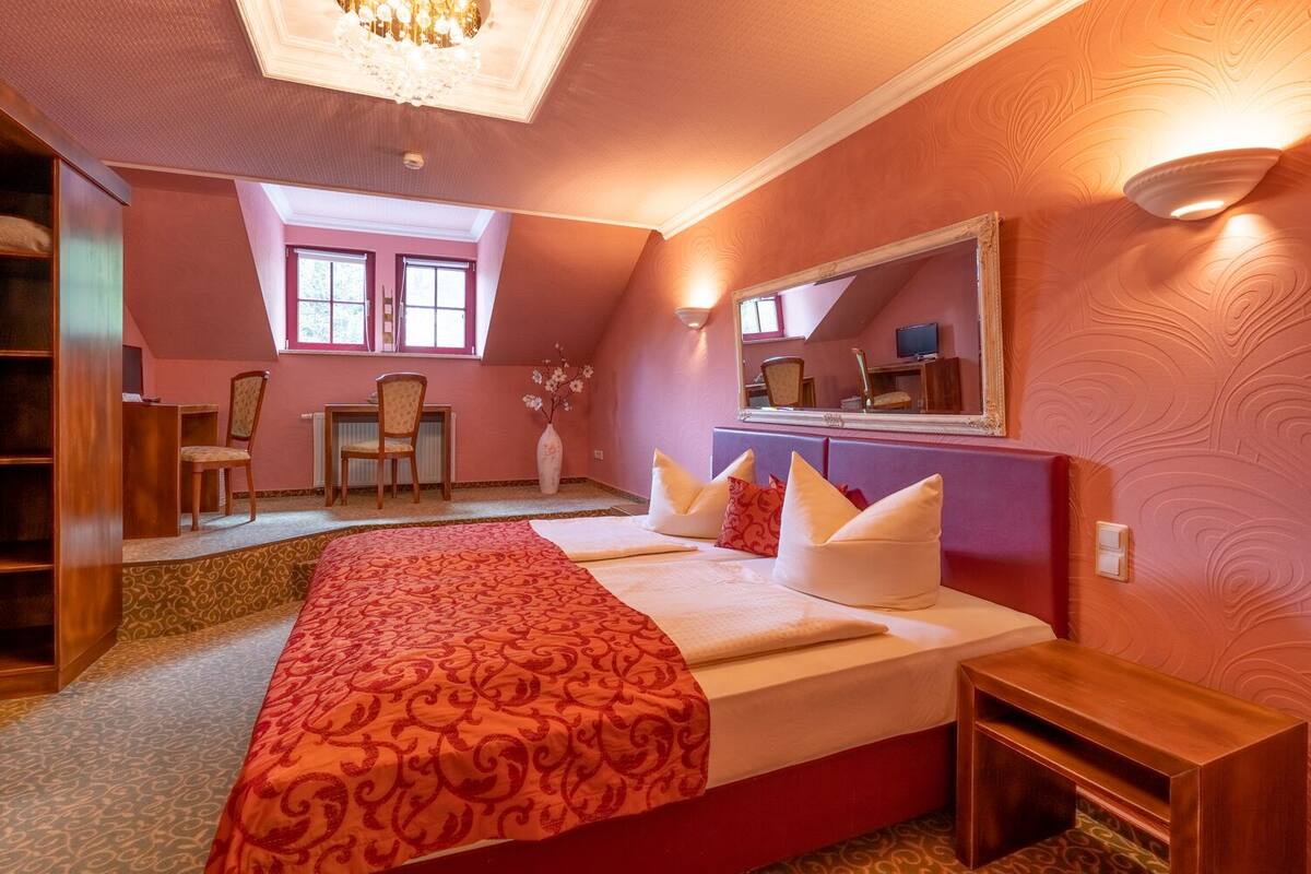 A bedroom with a large bed, a desk, a chair, and a mirror.