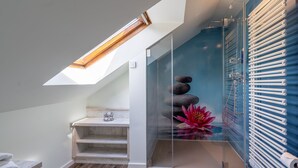 A modern bathroom with a skylight, a glass shower enclosure, a wooden bench, and a decorative flower arrangement. - Berggasthof Butterberg (Bischofswerda)