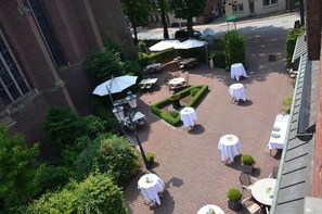 An outdoor patio area with tables and chairs, surrounded by greenery and a brick pathway.