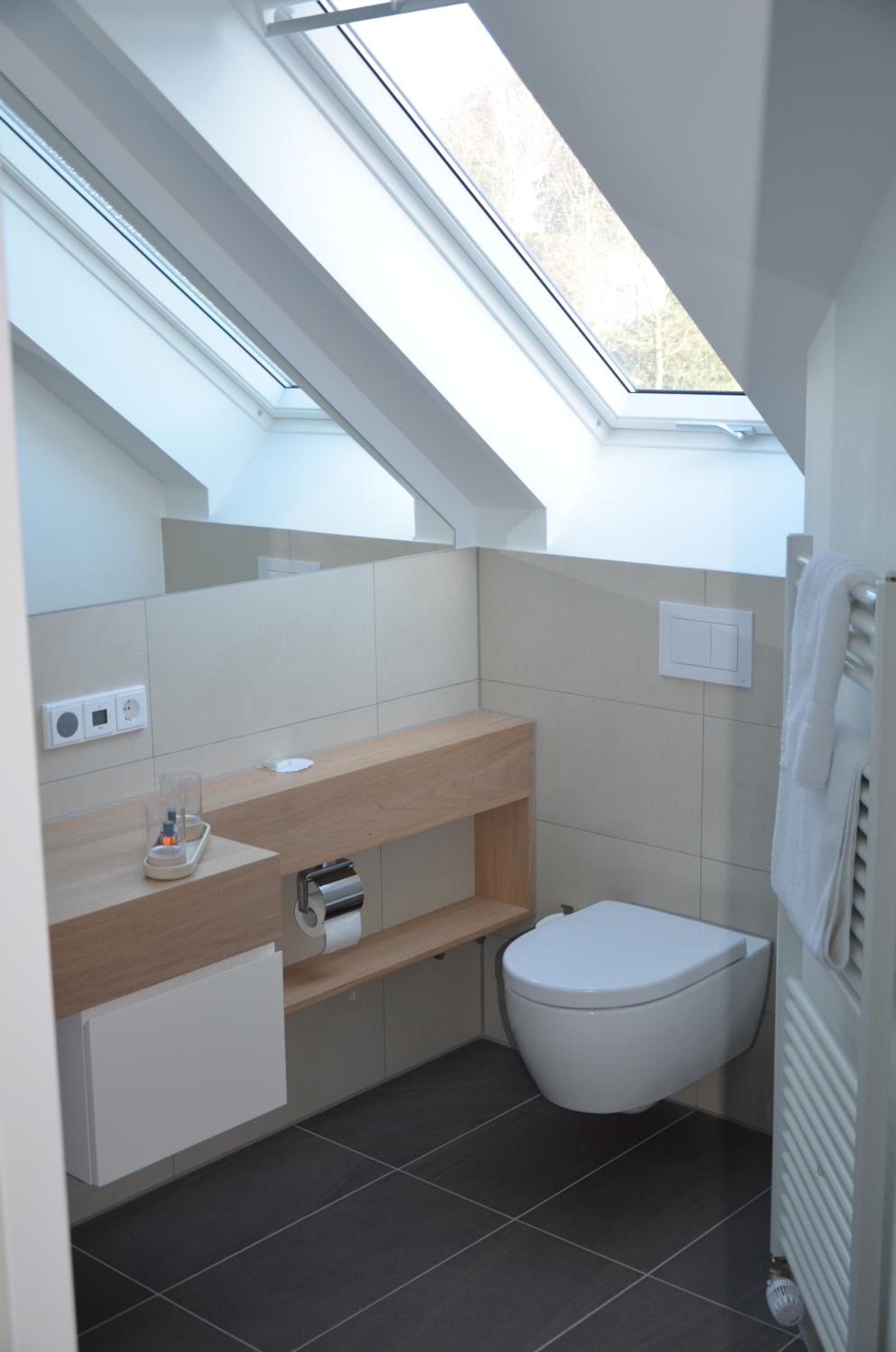 Ein modernes Badezimmer mit Dachfenster, Toilette, Waschbecken mit Spiegel und Handtuchhalter.