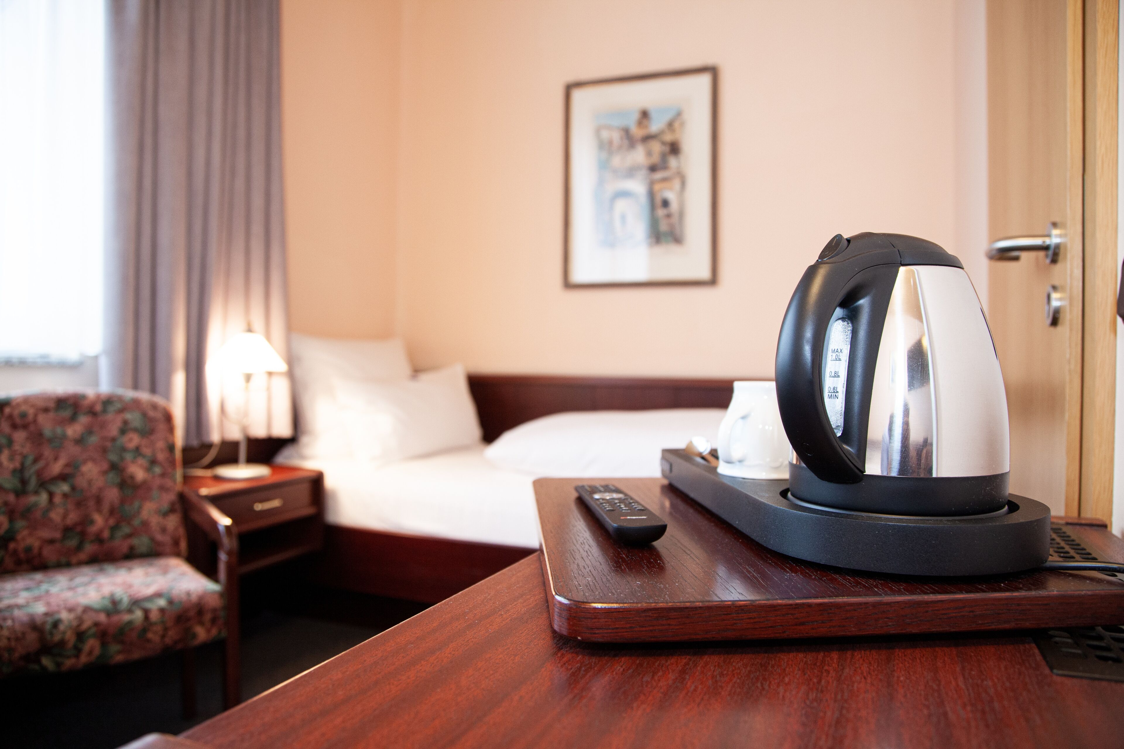 Een hotelkamer met een bed, een afstandsbediening, een waterkoker en een bloemenstoel.